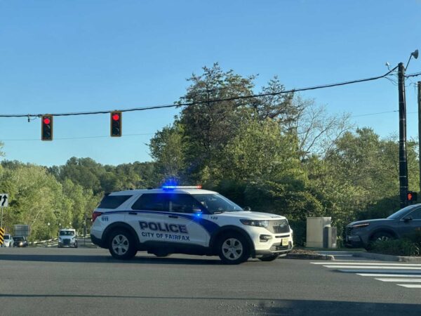 Police SUV from City of Fairfax with flashing blue lights blocking an intersection under a clear blue sky.