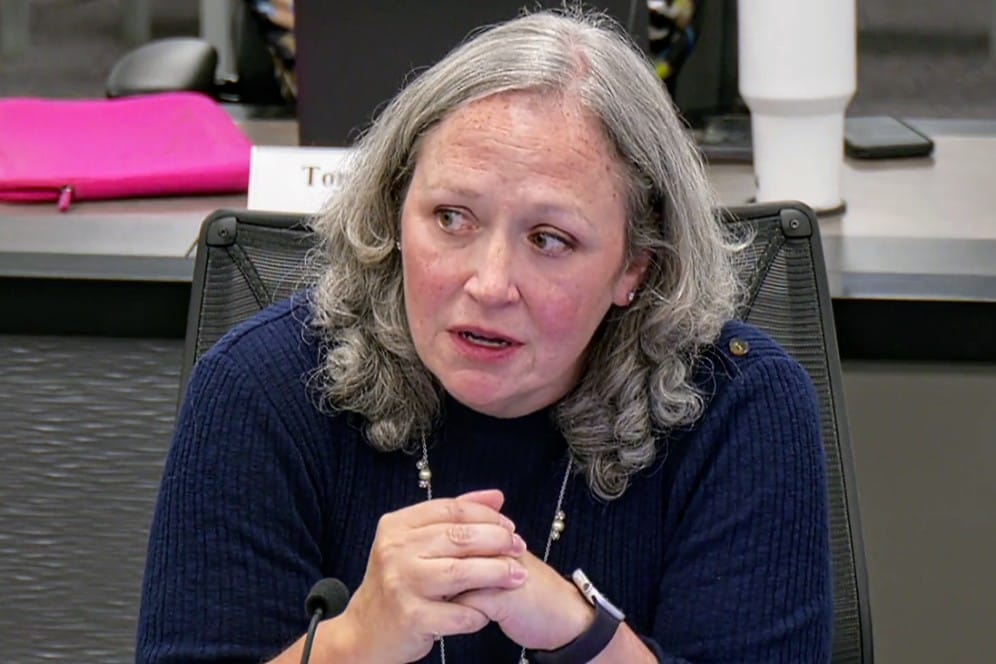Fairfax County Chief Financial Officer Christina Jackson (screenshot via Fairfax County) | FFXnow Middle-aged woman with gray, curly hair in a navy sweater sits at a conference table, hands clasped, speaking into a microphone.