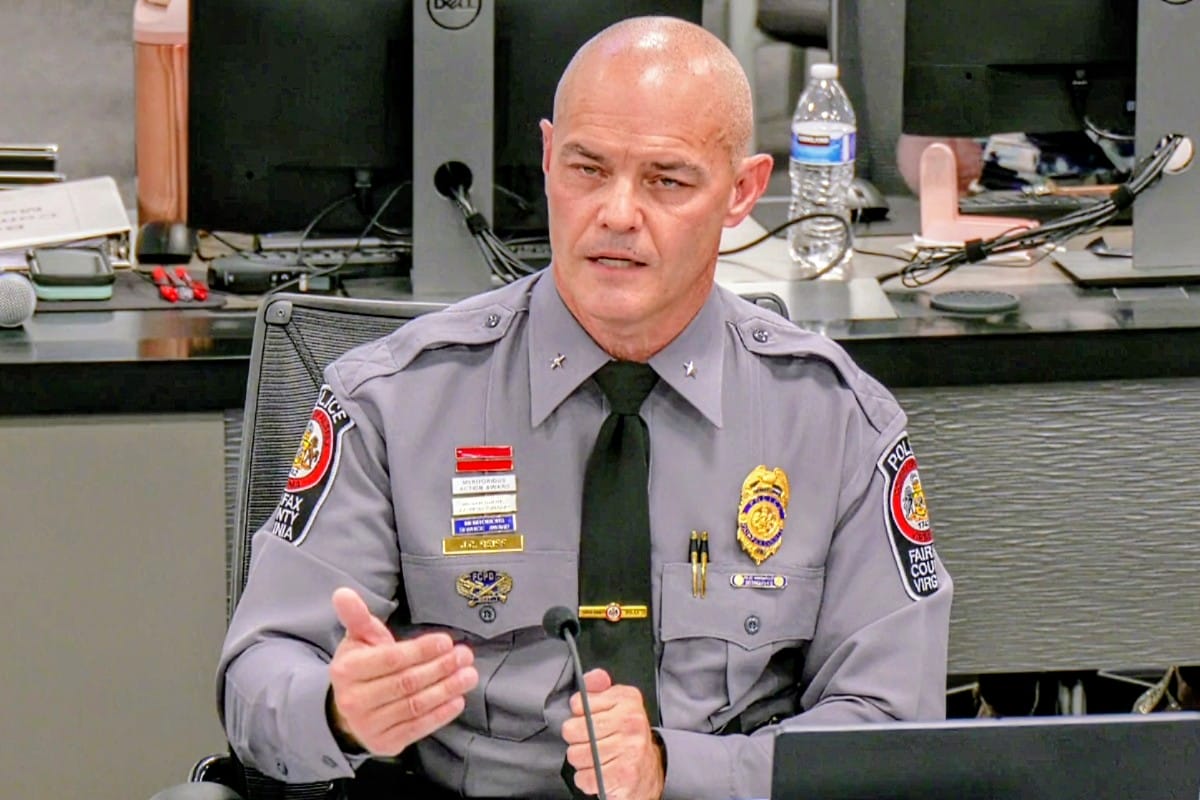 Fairfax Deputy Chief of the Operations Support Bureau Jeffrey Reiff (screenshot via Fairfax County) | FFXnow Bald male police officer in a gray uniform with medals sits at a conference table, gesturing as he speaks into a microphone.