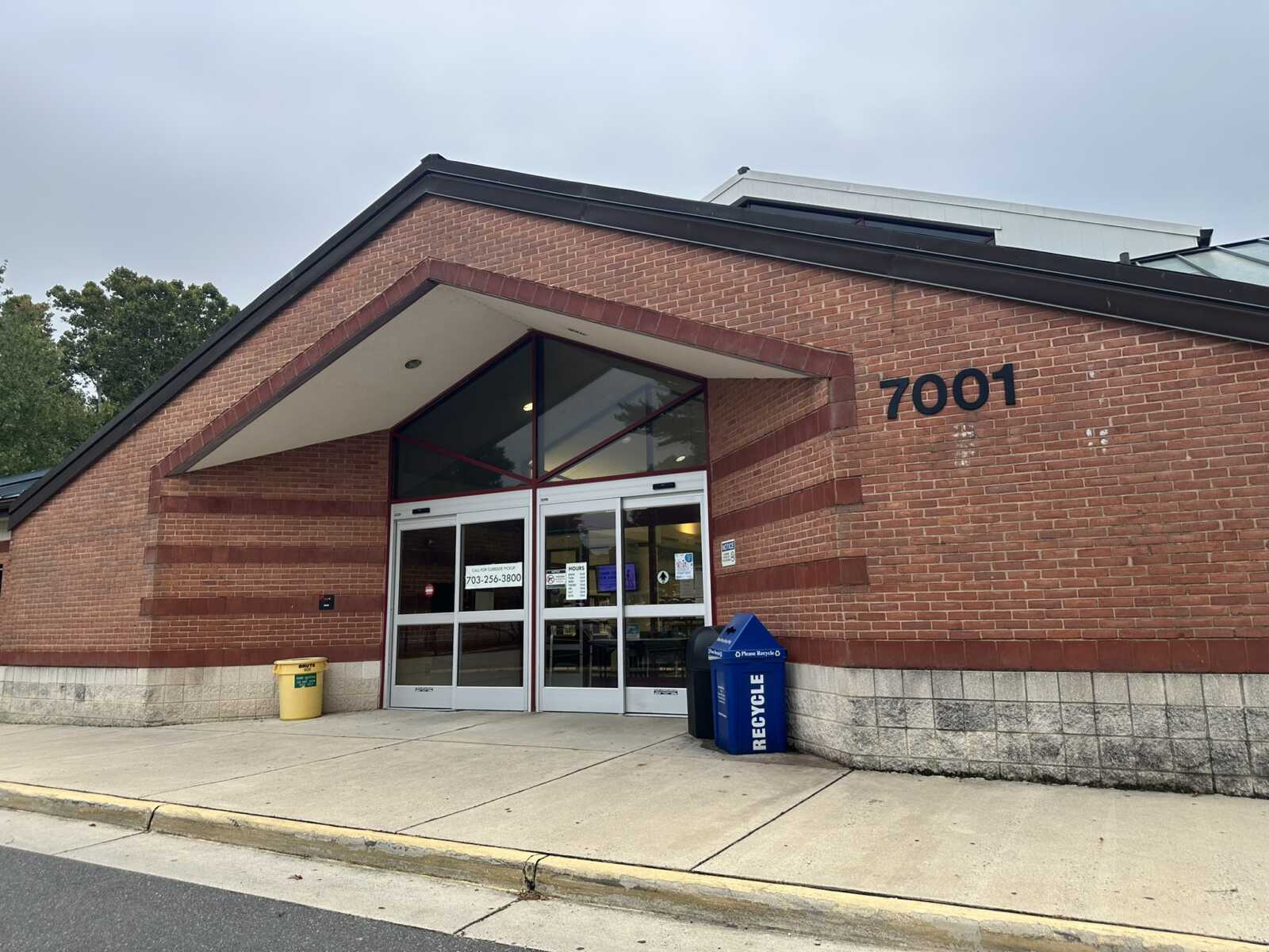 Brick building entrance with glass double doors, under a triangular red-brick awning, address 7001 on the wall.