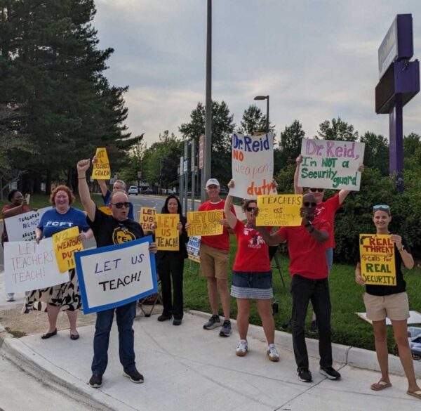 Group of protesters on a sidewalk holding colorful signs about teaching and security.