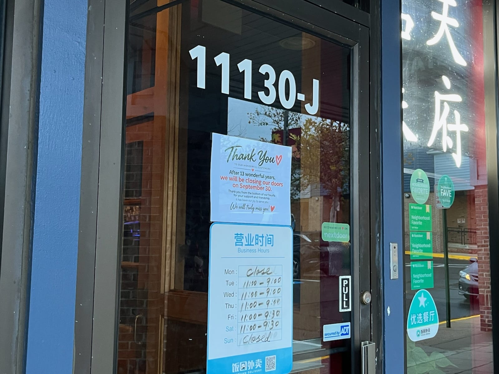 storefront door with large '1130-J' numerals and a 'Thank You' card announcing closure on September 30; blue business-hours flyer lists Mon-Sun hours in Chinese and English