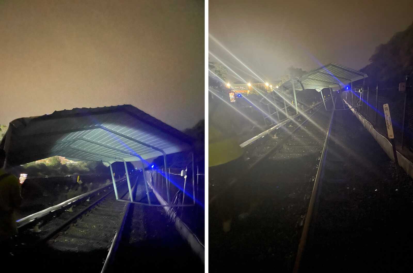 Nighttime view of a damaged metal canopy over railway tracks, with blue emergency lights in the distance and a hazy sky.