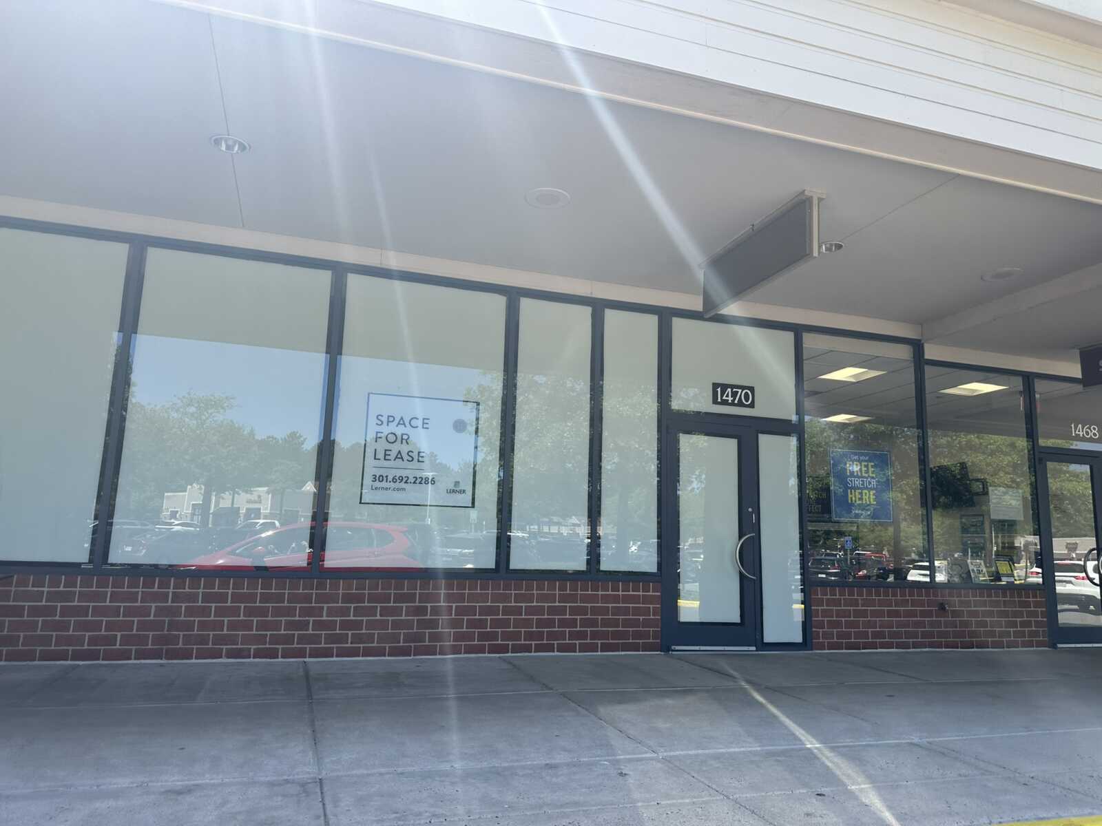 Storefront with large glass windows and brick base; 'Space for Lease' sign in the window, 1470 address above door, sunny glare.