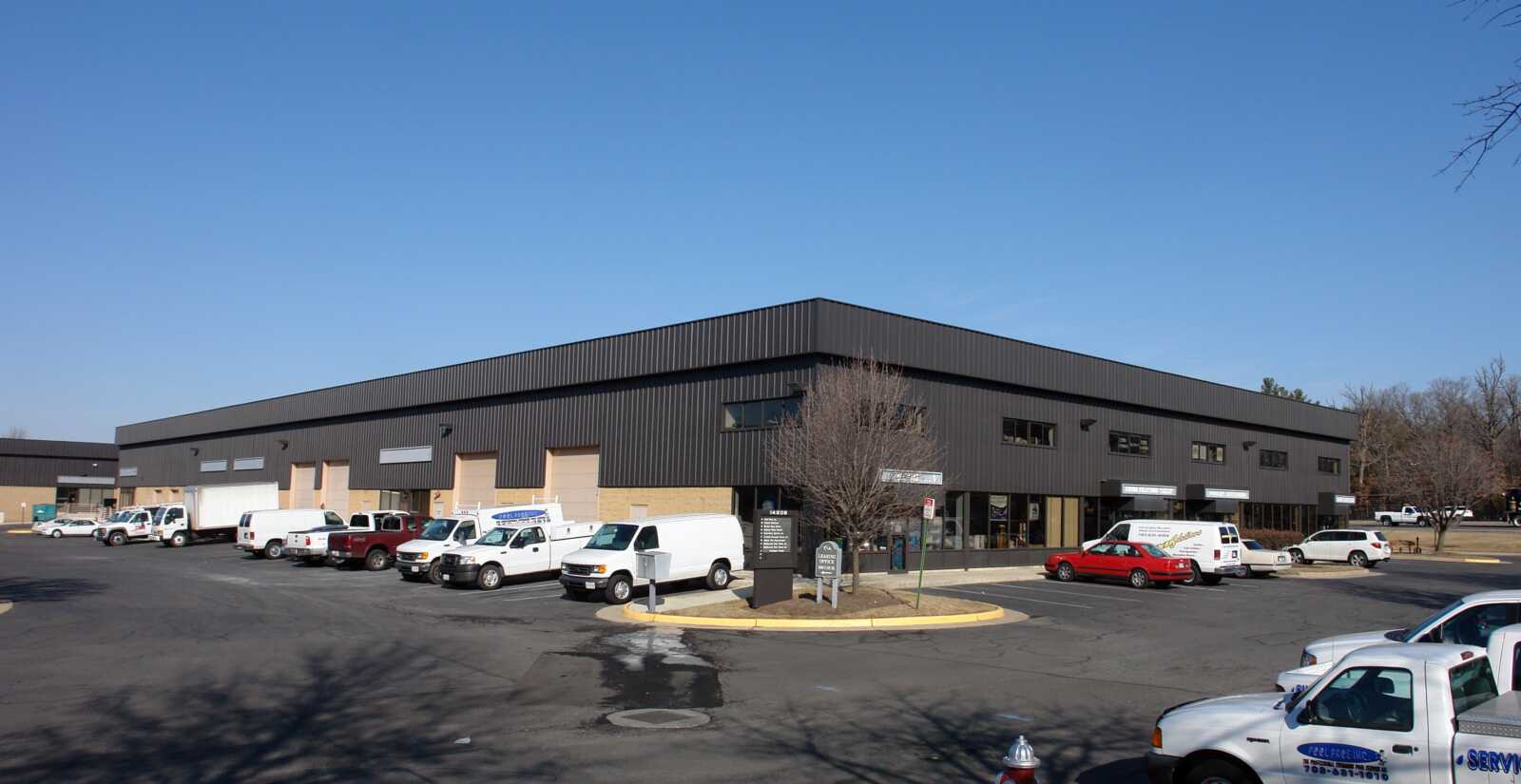 Exterior of a modern black metal warehouse with several loading bays and a row of white cargo vans in the parking lot.