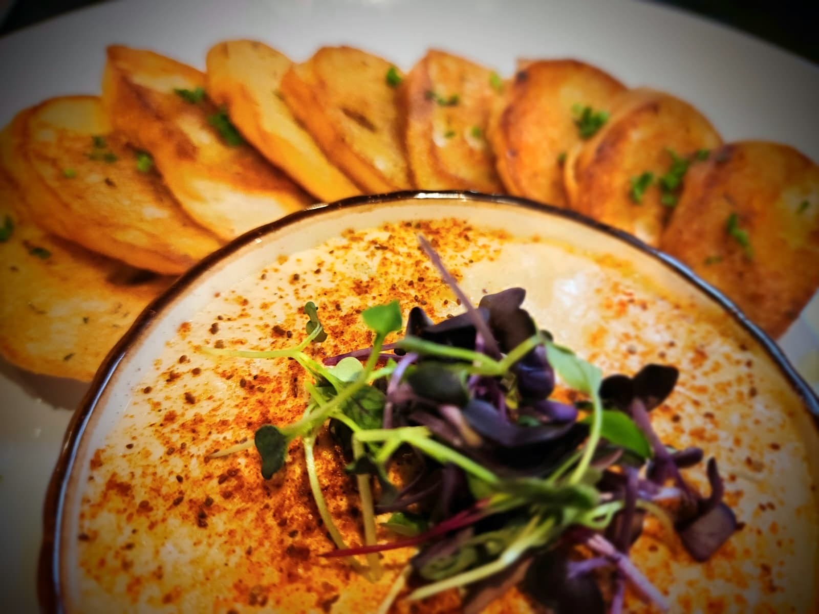 Creamy dish topped with paprika and microgreens, surrounded by toasted bread slices on a plate