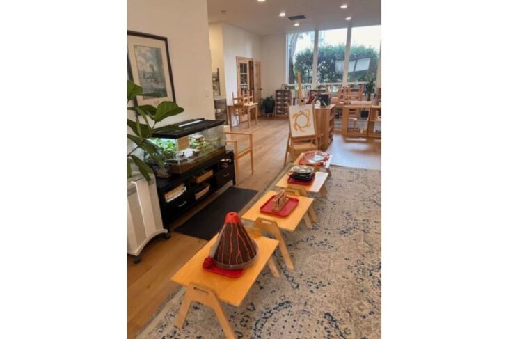 Bright craft studio with low wooden tables displaying handmade projects in a sunlit room with shelves and large windows.