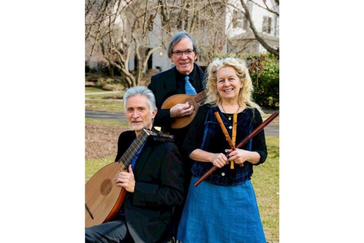 Three senior musicians pose outdoors with their instruments: a man with a lute-like instrument, a man in back with a small guitar/mandolin, and a woman holding two wooden flutes, all smiling.