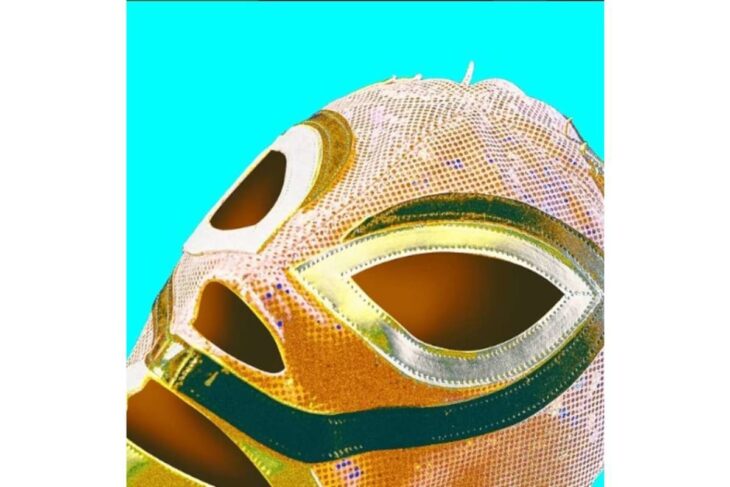 Close-up of a colorful lucha libre mask with orange, gold, and green details against a bright cyan background