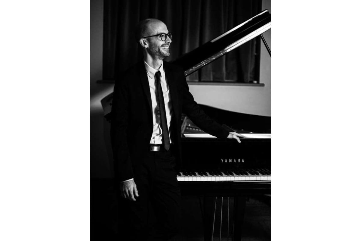 Smiling man in a suit standing beside a Yamaha grand piano.