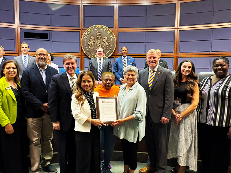 The Fairfax County Board of Supervisors presents a proclamation honoring the 25th anniversary of the Reston Multicultural Festival. (Courtesy Fairfax County) | FFXnow Group of smiling people posing for a photo, with two people holding a plaque in the middle.