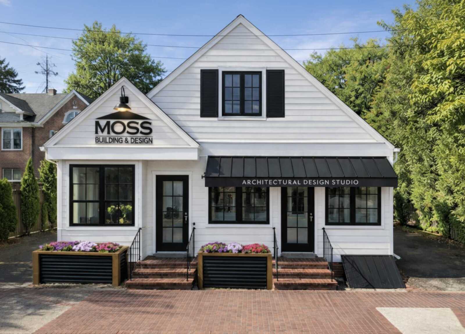 Front of Moss Building & Design architectural studio, a white two‑story storefront with black trim, planters, and a black awning reading 'ARCHITECTURAL DESIGN STUDIO'