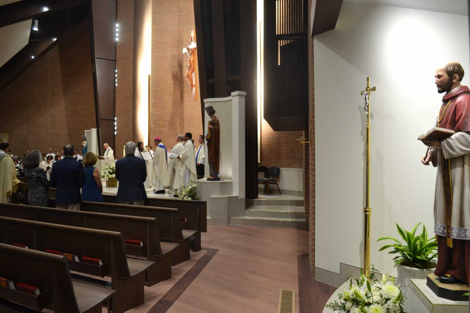 Congregation standing for Mass inside a brick church with clergy in white robes at the altar.