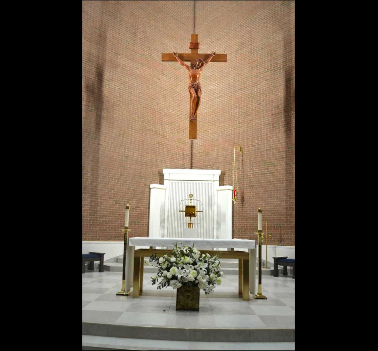 Our Lady of Good Counsel's altar was rebuilt with surrounding stone flooring and a tabernacle as part of a renovation project (staff photo by Mary Stachyra Lopez) | FFXnow Crucifix above a white altar in a brick church, with a floral arrangement at the front.