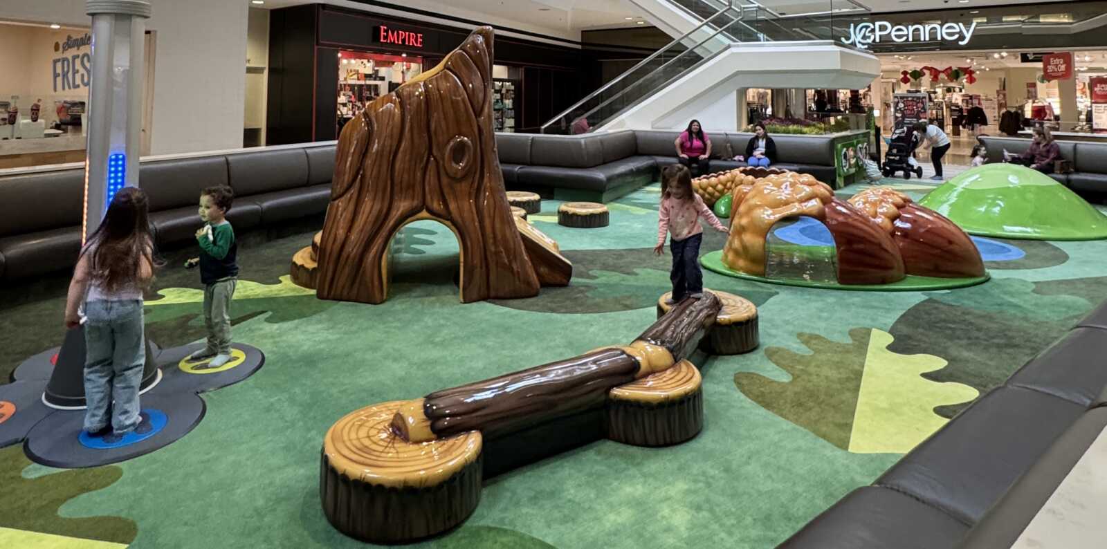 Children play on a green carpeted area with nature themed indoor playground equipment