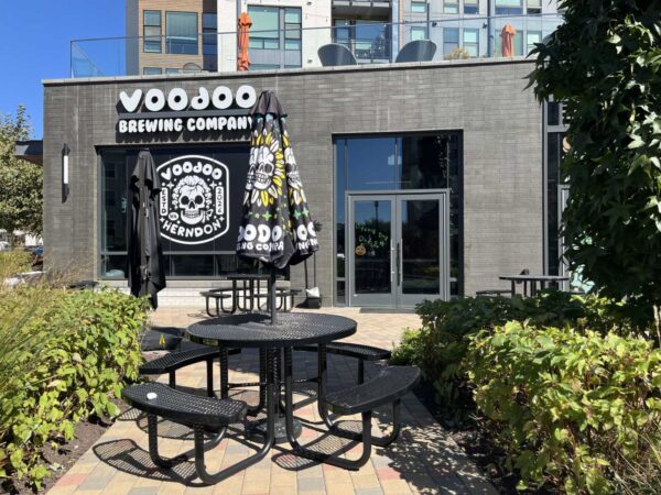 Outdoor seating area in front of Voodoo Brewing Company with round black tables and closed umbrellas on a sunny day.