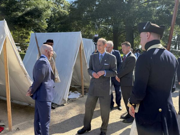 Group of men, including a suited gentleman, standing near canvas military tents at an outdoor historical reenactment.
