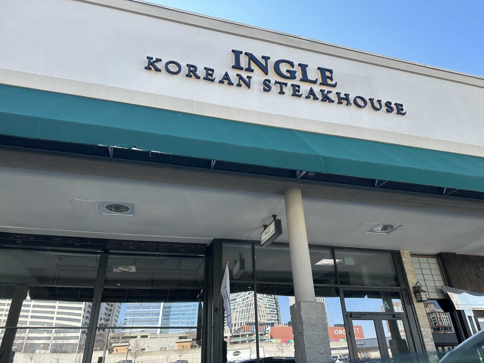 Facade of a Korean steakhouse storefront with a teal awning and large sign that reads 'INGLE KOREAN STEAKHOUSE' against a clear blue sky.