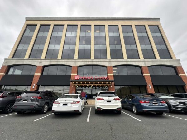 Front view of a brick-and-glass building with large vertical windows; entrance for Mama Chang restaurant with red sign and black awnings, cars in the parking lot fronting the building.