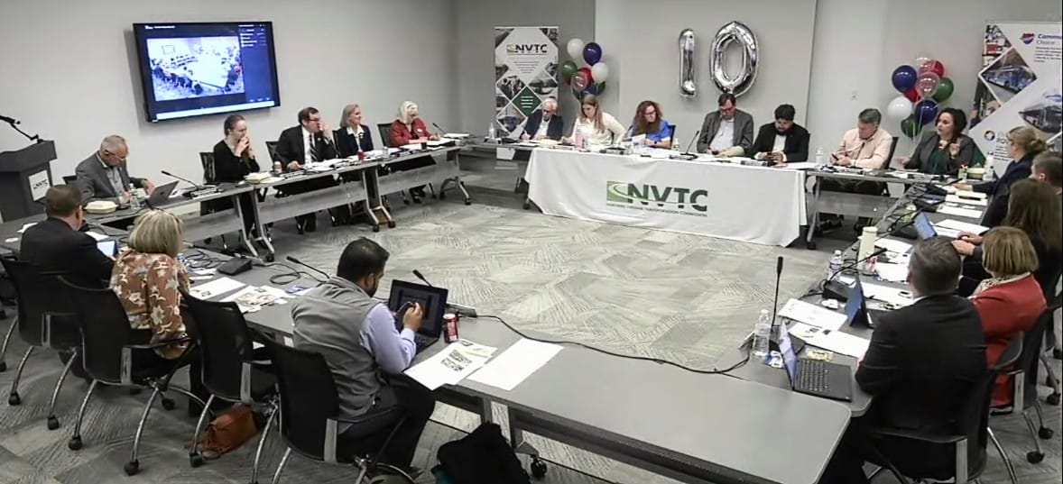 Oct. 1, 2026, Northern Virginia Transportation Commission meeting (screenshot via NVTC) | FFXnow A large conference room with people seated around a U-shaped table, an NVTC banner at the center and silver '10' balloons in the back, as they discuss documents.