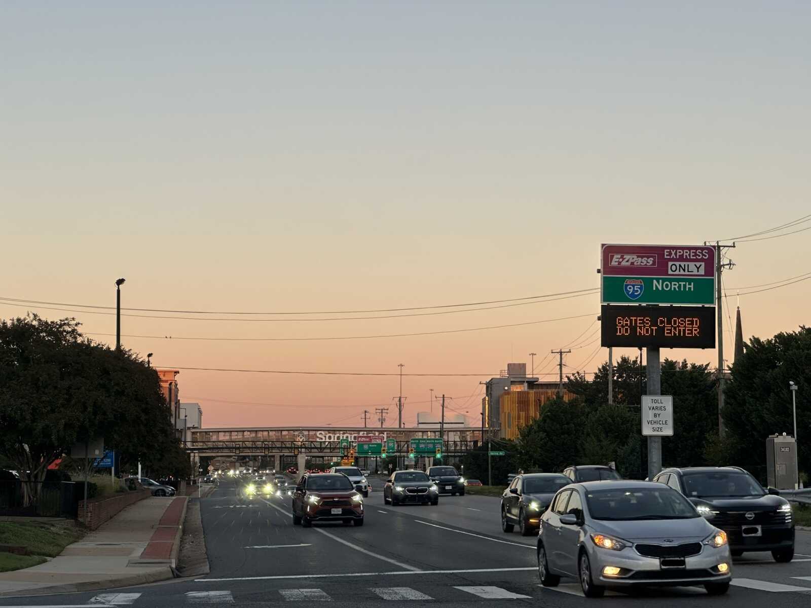 Old Keene Mill Road near the Springfield commuter parking garage pedestrian bridge at sunset (staff photo by Angela Woolsey) | FFXnow Urban highway at sunset with cars in traffic and a large roadway sign showing I-95 North; electronic message reads 'GATES CLOSED DO NOT ENTER'