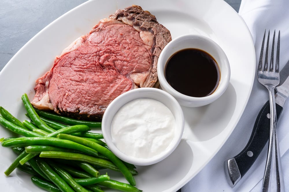 Juicy beef steak with green beans and two dipping sauces on a white plate (brown and white sauces).