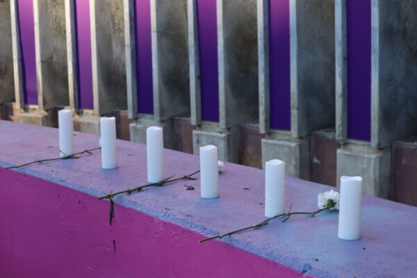 Row of white pillar candles placed along a purple concrete ledge, with green stems and small white flowers between them.