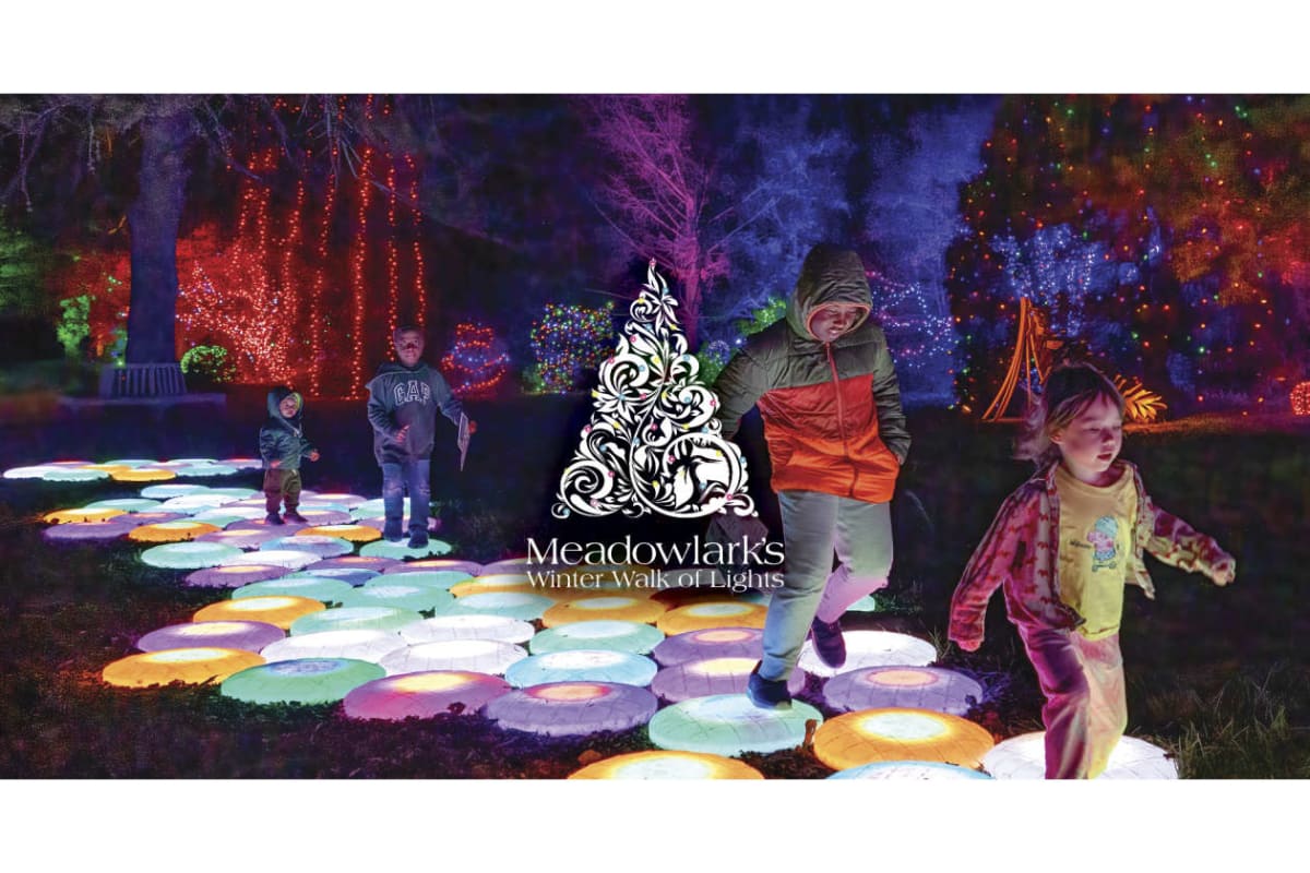 Children walking on glowing circular light tiles in a nighttime garden, with colorful holiday lights and Meadowlark's Winter Walk of Lights logo at the center.