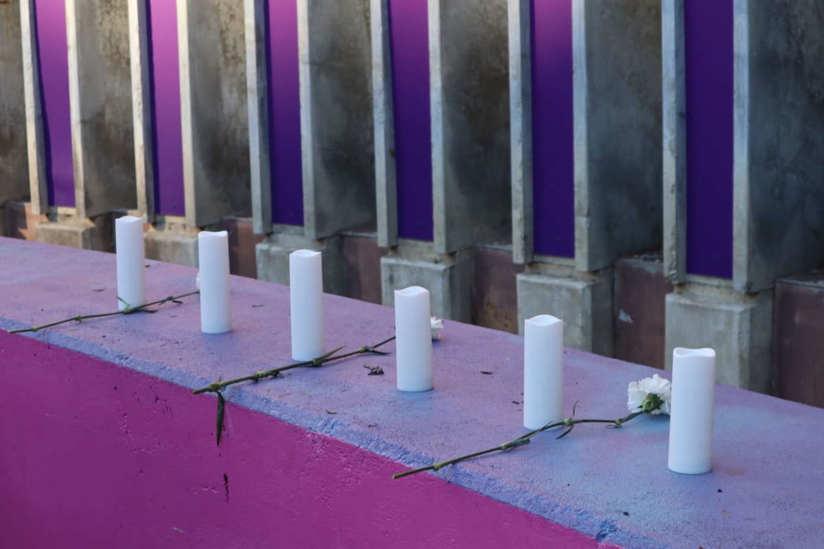 White pillar candles lined along a purple ledge, with small white flowers and green stems, against a wall with purple panels.