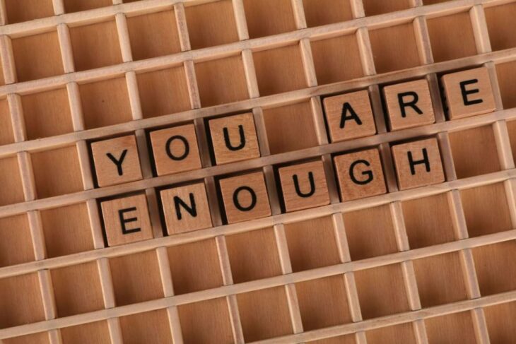 Wooden letter tiles spell 'YOU ARE ENOUGH' on a grid tray.
