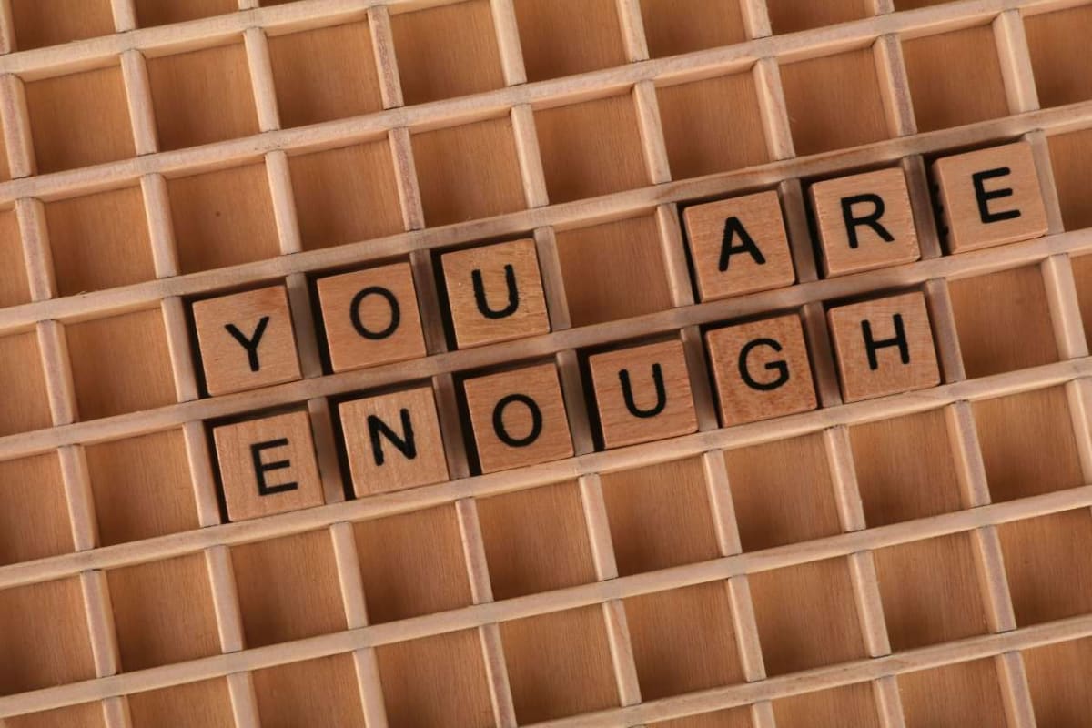 Wooden letter tiles spell 'YOU ARE ENOUGH' on a grid tray.