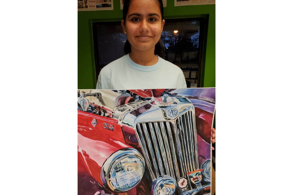 Girl in a light blue shirt smiles as she holds a large painting of a vintage MG car front image.